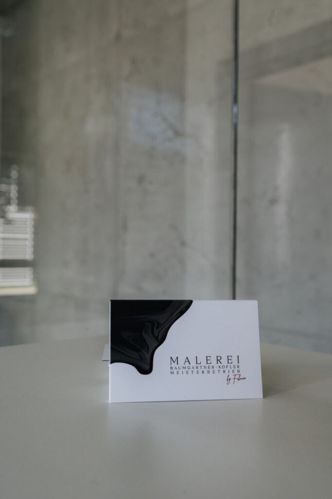 Visitenkarte der Malerei Baumgartner-Kofler vor einer Betonoptik-Wand